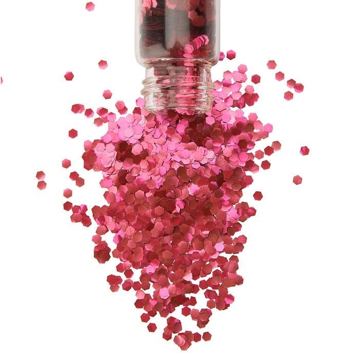 Red chunky biodegradable glitter in a glass jar tipping out onto a white background.