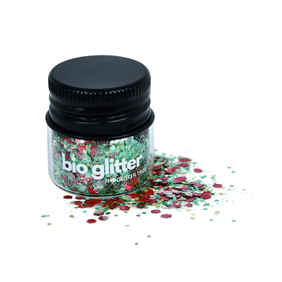 Christmas tree themed glitter in a glass jar with a lid, glitter is spilled on serface.