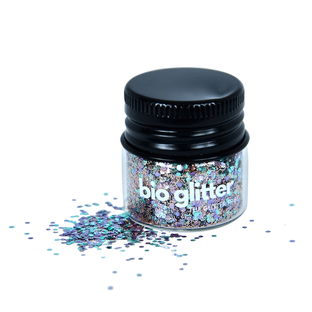 Turquoise and mauve fine bio glitter in a glass jar on a white background.