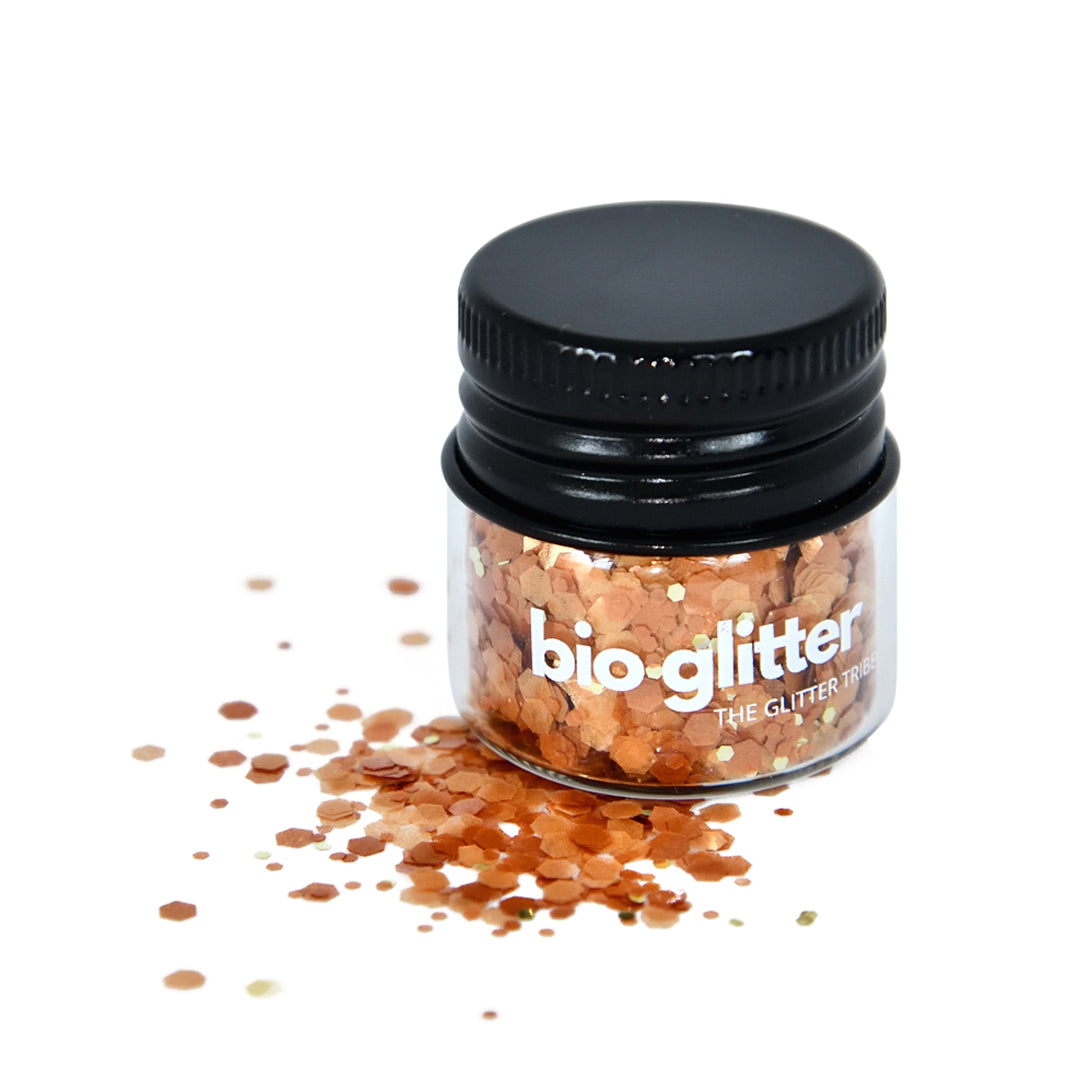 Gold and yellow toned bioglitter in a glass jar with a black lid with some glitter at side on a white background.