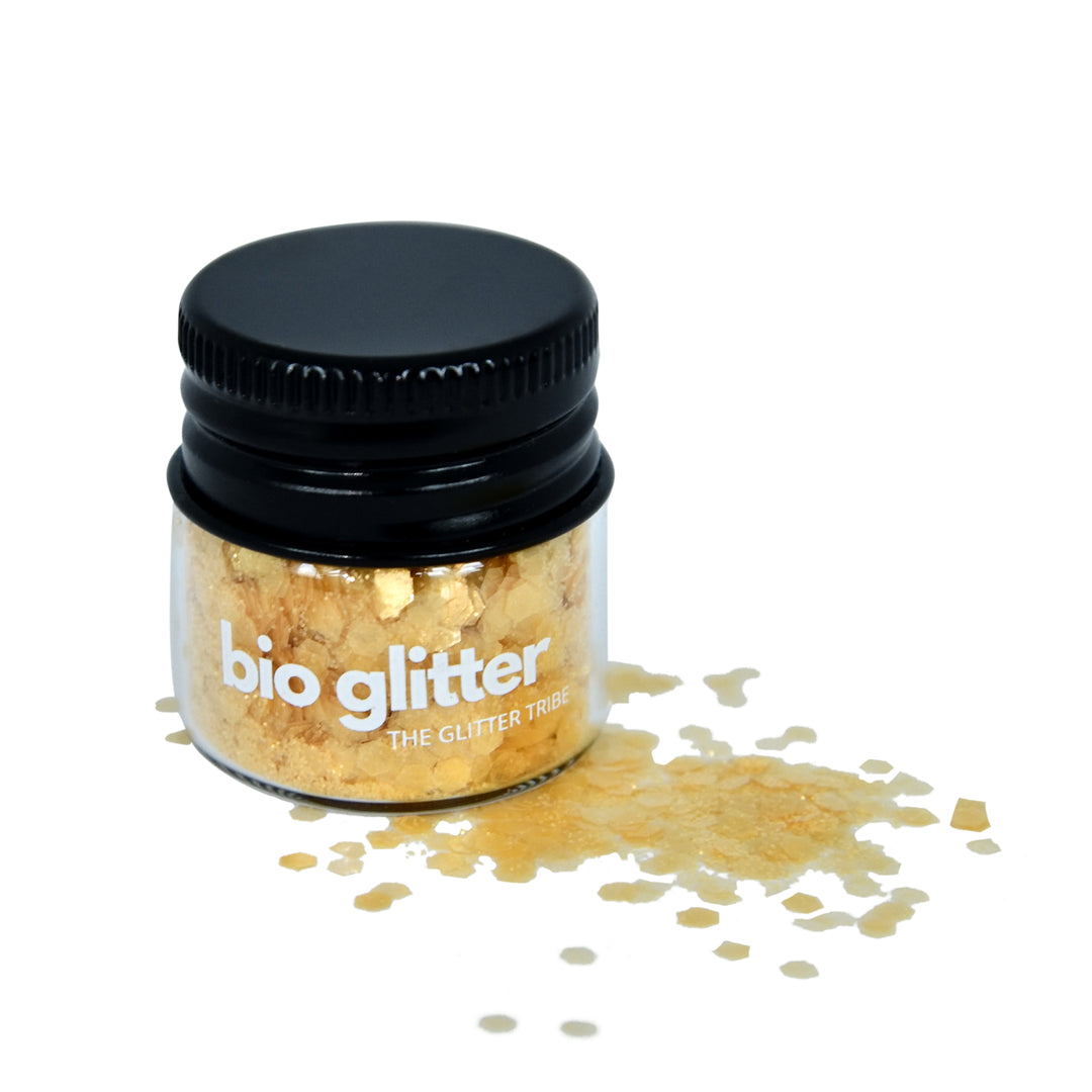 Yellow chunky bioglitter in a small glass jar with a black lid some glitter sitting next to jar on side,